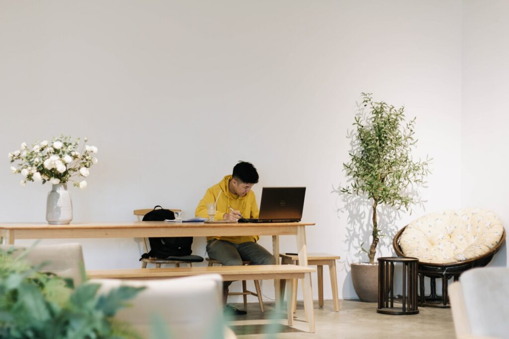 A person sat at a kitchen table in a large open looking living room. Maybe this is part of the best work from home routine?