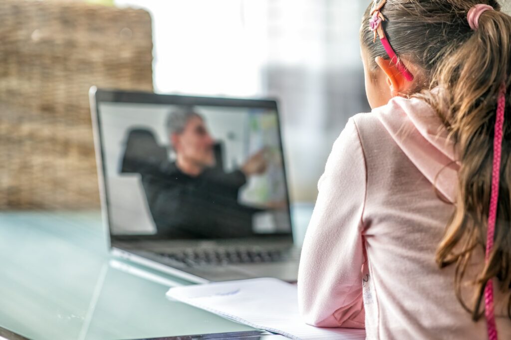 A child looking at a laptop with a teacher on screen online teaching.