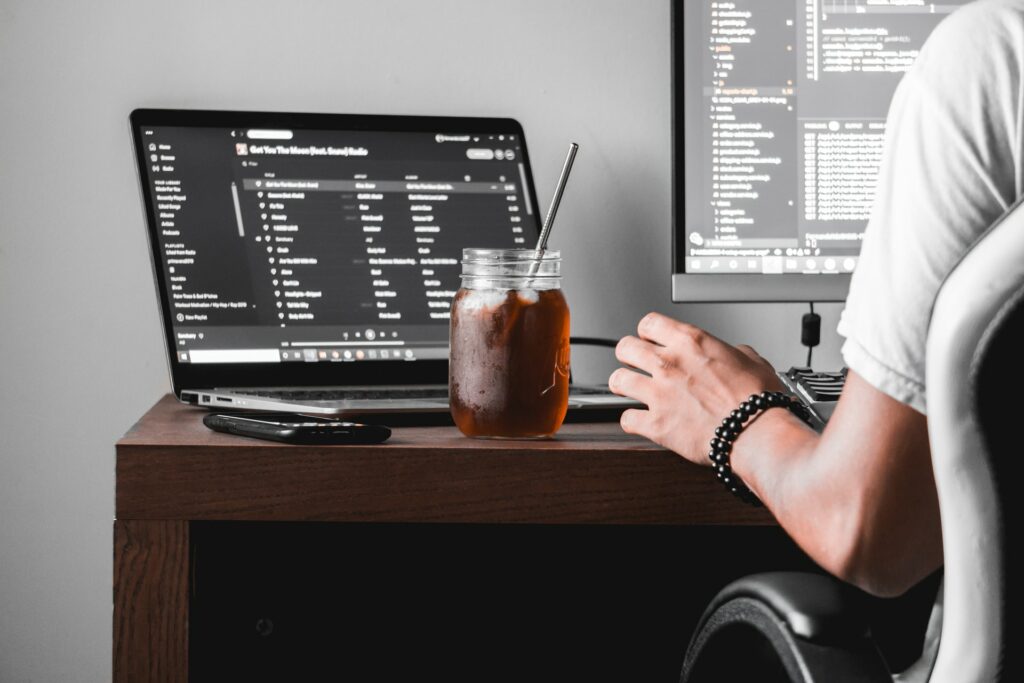 A laptop is connected to a monitor with a glass on a desk using a metal straw say next to a phone looking for the best calendar app.