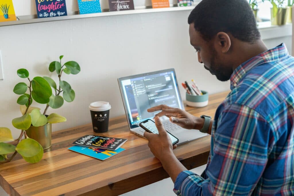  A person in front of their laptop wioth tabs for the digital office open as they also check their phone while working from home.