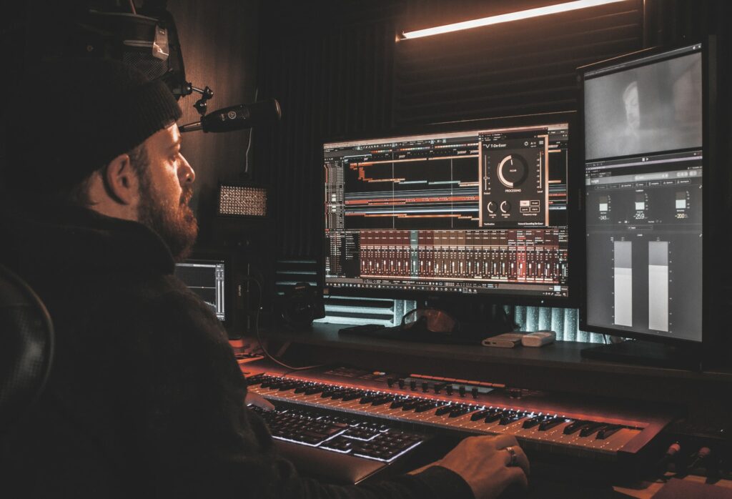 A person using VSTs for live streaming at a large Digital audio computer with two screens, a mic and a large musical keyboard.